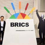 Alissa Wang, Angela Hou, and Ian Stansbury stand beside sign at 2018 BRICS Summit
