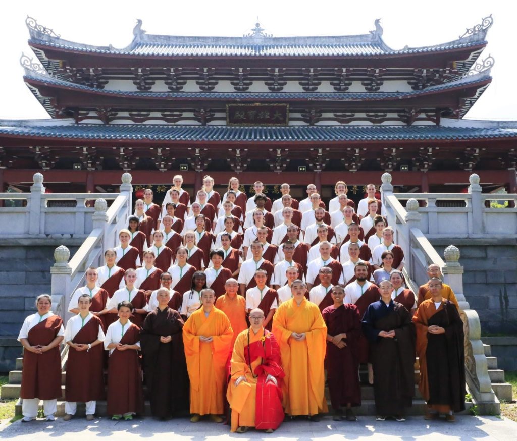 A group of buddhist monks stands in front of a temple.
