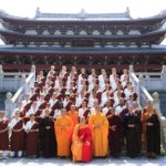 A group of buddhist monks stands in front of a temple.