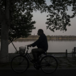 man rides bicycle by lake with mask on
