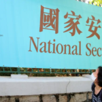 woman wearing mask looks up at sign with Chinese characters and English message that says "National Security Law"