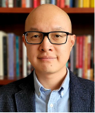 photo of Sida Liu wearing glasses in front of a background of books.