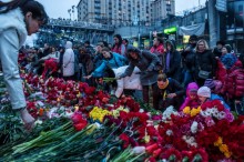 A photograph of people in Kiev laying flowers on the improvised memorial to the victims of shootings on the background of the slogan: "the revolution must go on"