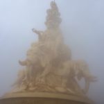 a golden statue is shrouded by mist.