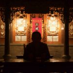 A man sits in shadow with a temple illuminated behind him.