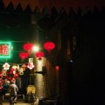 A man rides a bicycle through a dark alley lit by signs and red lanterns.