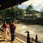 two women in kimonos look from a covered porch onto a zen sand garden.