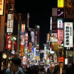 At night in Tokyo, the street is lit up with colourful signs and people fill the street.