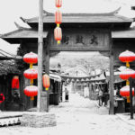 A gate flanked by red lanterns provides an entrance to a traditional village street.