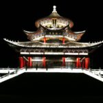 a Chinese temple is lit up from below against a black sky.