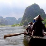 people ride in a small wooden boat with paddles through Ha Long Bay