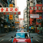 a taxi drives down a street filled with signs in Hong Kong.