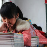 a girl yawns in front of a stack of books