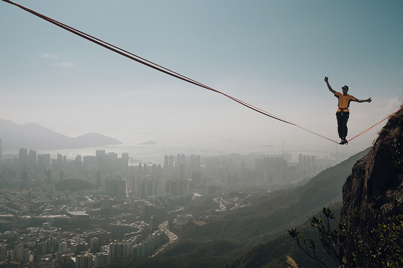 Melody (Chi Lok) Chan's photo, Lion Rock Spirit. The photo shows a figure balanced on a line suspended across Lion Rock mountain high above the misty skyline of Hong Kong.