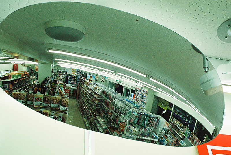 Photo in Andy Takagi’s “Summertime in Tokyo” series; the image shows the inside of a convenience story from a curved mirror