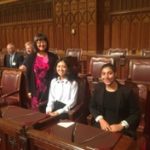 Munk One student Nika sits with another UofT student in the House of commons as Senator Yonah Martin stand beside them.