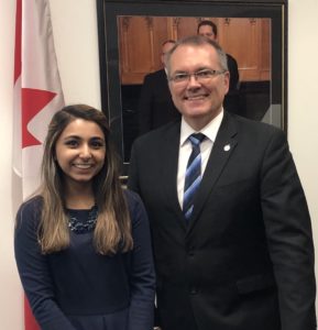 Student Fayha poses with MP Luc Berthold of Mégantic in front of a Canadian flag and a painting