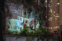 Rectangular art photograph showing collage of urban apartment buildings with a laundry line and human figure in a red shirt in lower left foreground