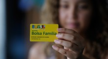 A young woman holds a Bolsa Familia membership card to the foreground.