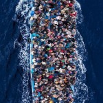 A large boat containing hundreds of people swims in the floats in the middle of the ocean.