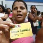 A woman standing in a crowd of people holds up a Bolsa Familia health care card.