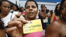 A woman standing in a crowd of people holds up a Bolsa Familia health care card.
