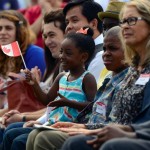 A little girl sits on her cousin's lap waving a Canadian flag.