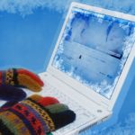 A pair of gloved hands typing on a frozen laptop.