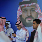 Young Saudis chat by a poster of Saudi Crown Prince Mohammed bin Salman during a tech forum in Riyadh