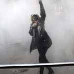 A university student attends a protest in Tehran University while a smoke grenade is thrown by Iranian police.