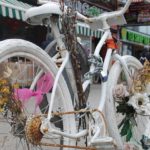An all-white bike adorned with flowers in a makeshift memorial on a street corner