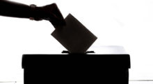 A silhouette of a hand putting a voter ballot into a box