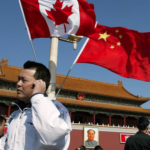 Man on phone standing in front of Canada and China flags