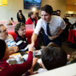 Justin Trudeau shaking the hand of a woman sitting in a diner booth