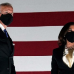 Joe Biden and Kamala Harris pose in front of the American flag, wearing masks.