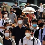 A crowd of masked people walking down the street in Tokyo, Japan