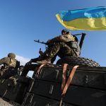 Ukrainian sitting on top of a tank bearing the flag of Ukraine