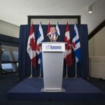 Mayor John Tory gives a speech in Toronto, with a podium that has the city logo. the flags of Ontario and Canada are behind him.
